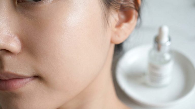 Gros plan sur le visage d'une femme avec une peau saine près d'un flacon de sérum sur une soucoupe.