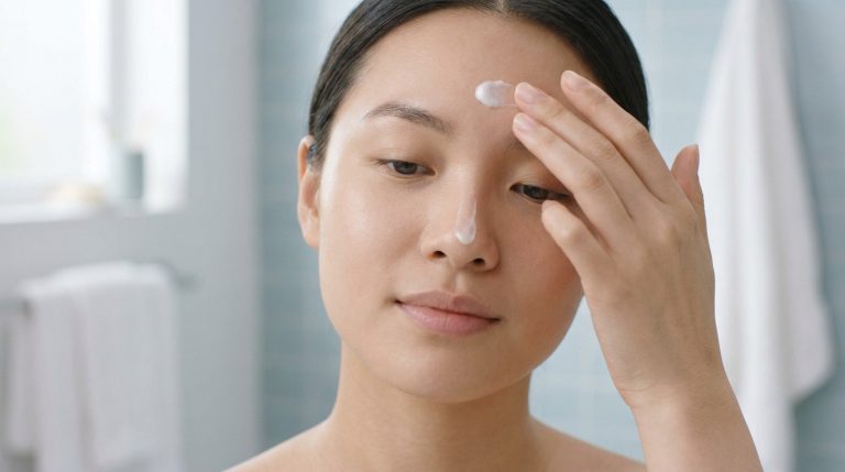 Jeune femme appliquant de la crème hydratante sur son visage dans une salle de bain.